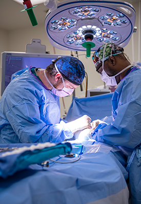 Two providers performing surgery. They are wearing protective gear: surgery caps, face masks, surgery gowns and surgery gloves.