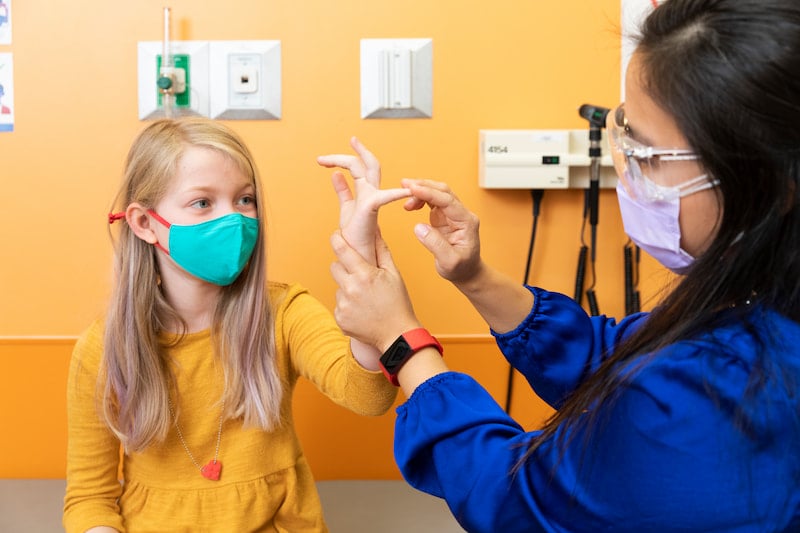 A female clinician bends the finger of a female patient during a physical exam at the Children's Mercy Genetics Clinic.