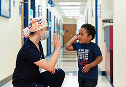 Dr. Rebecca Rentea wearing a face mask and scrub hat high-fiving Taitum Ellis.