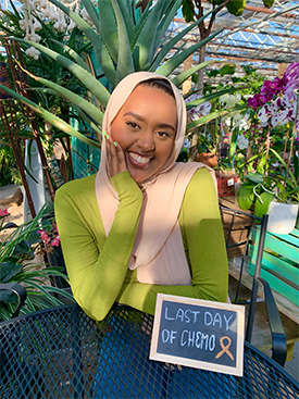 Munira Nuru smiling and sitting in back of a sign that reads, "Last day of chemo."