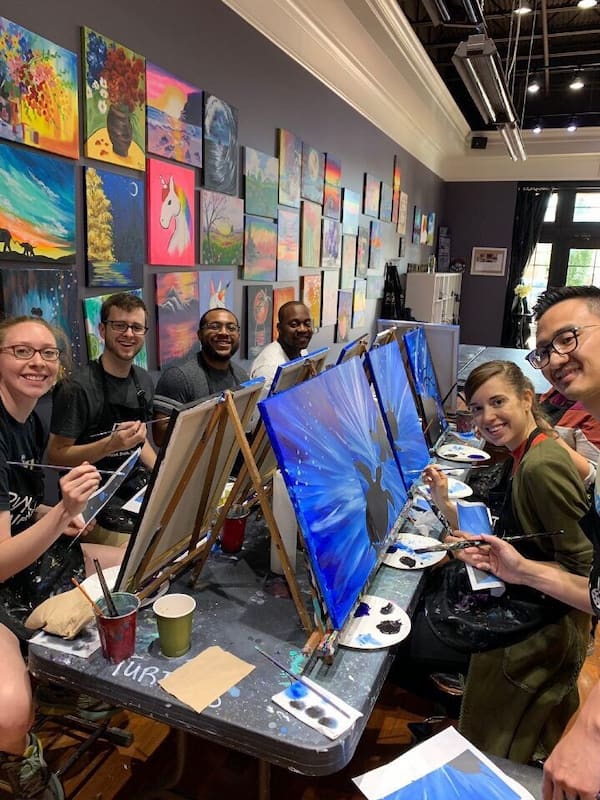 Several young adults sit together at a table in a painting cafe.