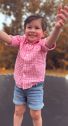 Elijah smiling and jumping on a trampoline outside.