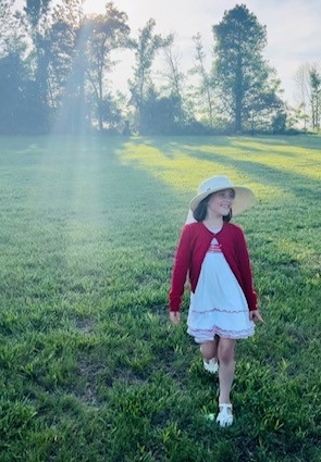 ella in a dress and hat outside in the grass