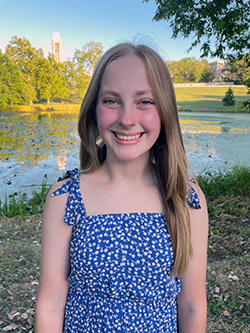 Bailey standing outside, in front of a lake and smiling.