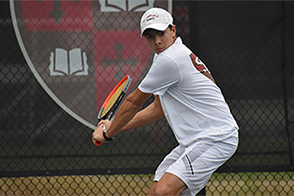 Nathan Turledove in a white tennis outfit and a tennis racket in his hands playing tennis.