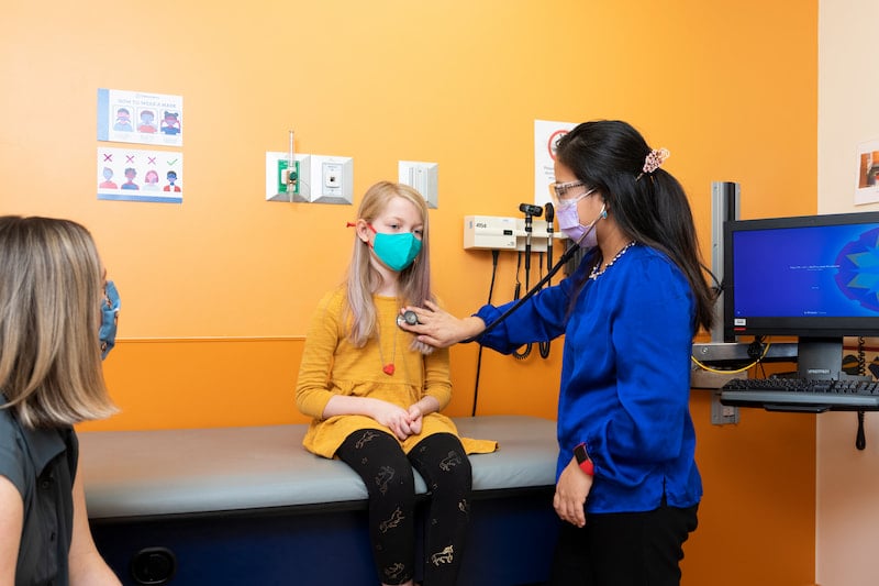 A female clinician uses a stethoscope on a female patient at the Children's Mercy Genetics Clinic.