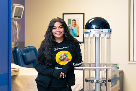 Children's Mercy Environment Services manager, Rachael Hughes, leaning against a TRU-D robot in the Research/Education Unit of Adele Hall.