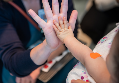 An adult hand and a child's hand high fiving.