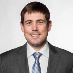 Thomas Champion smiling and wearing a shirt, suit jacket and tie.