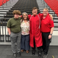 A family with a mom, dad and two teenage boys stand together at a graduation ceremony.