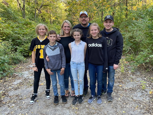 A family of 6 poses together in a wooded area