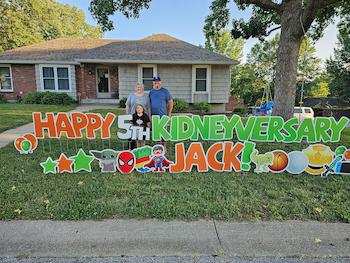 Jack and the family pose in front of yard sign they get annually to celebrate their Kindey-versary