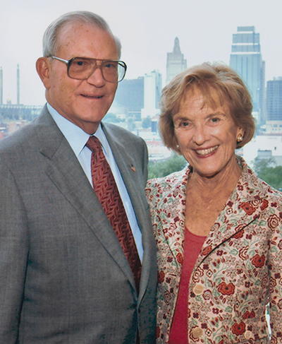 Color photo of Don and Adele Hall smiling with Kansas City skyline in the background.