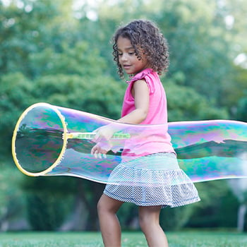 Young girl playing our side with a big bubble wand.