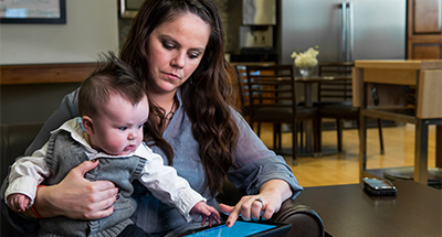 Mother with toddler on her lap. They are looking at a tablet device with the CHAMP app on it.