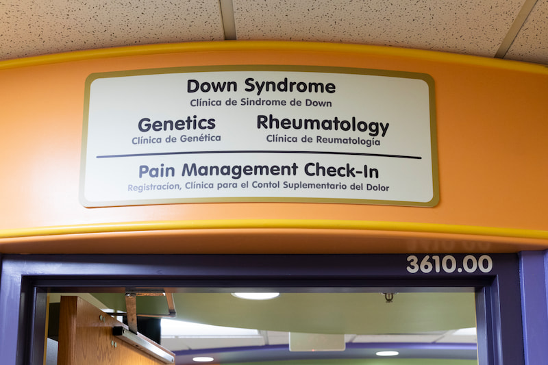 A sign welcomes you to the Children's Mercy Genetics Clinic. Other clinics include Down Syndrome, Rheumatology, Pain Management Check-in.