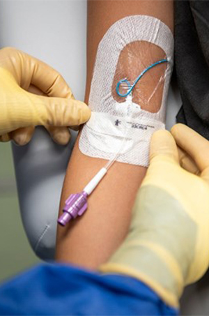 Two gloved hands of a nurse securing a PICC line in a child's arm at Children's Mercy.