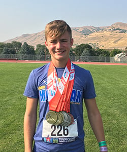 Brendan Elam at the Transplant Games. He is standing outdoors smiling with race number 226 on his shirt and 7 medals hanging around his neck.