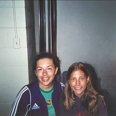 Two teenagers sit side by side at Camp Chimer, wearing casual clothing in an indoor camp setting.