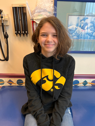 A teenage girl in a University of Iowa sweatshirt sits on an exam table