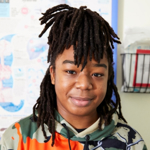 A teen boy with dreadlocks and a hoodie smiles at the camera
