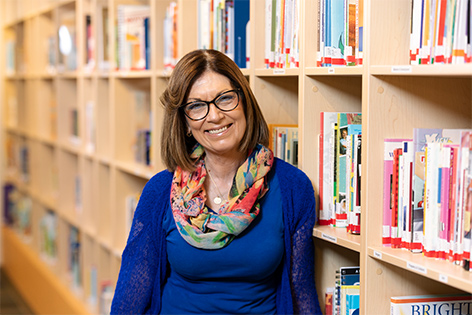 Alicia, Senior Medical Interpreter at Children's Mercy. She is smiling and leaning against a bookshelf filled with books in the Kreamer Library.