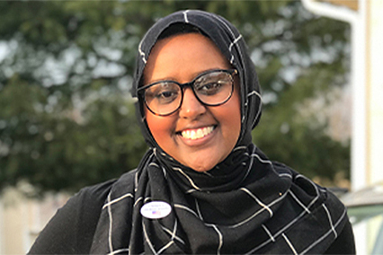 Munira Nuru smiling while wearing eyeglasses and a black colored hijab on her head.