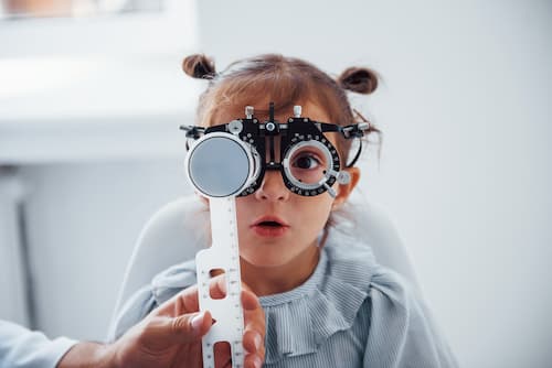 female toddler looking through phoropter lenses 