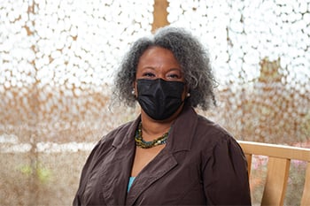 Melva Brownlee is sitting outside the chapel at Children's Mercy wearing a black face mask and smiling with her eyes.