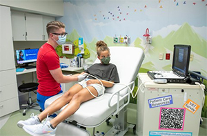 A young patient and a Children's Mercy nurse looking at the ultrasound of the patient's veins on a small computer screen.