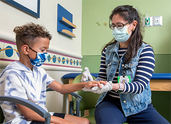 A Children's Mercy provider using a needle on a young patient to either do a joint injection or joint aspiration on the patient's wrist.