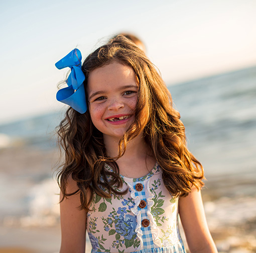 Little girl with blue ribbon in her hair smiling on the beach