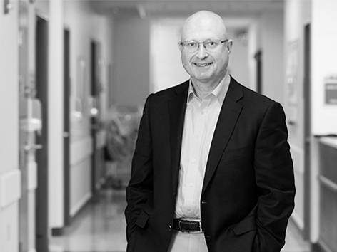 Black and white photo of CEO Paul Kempinski in Children's Mercy hallway smiling.