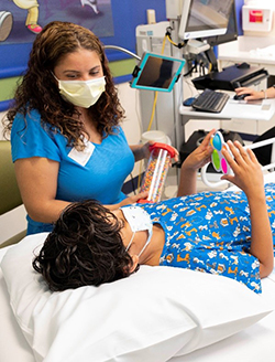 A Children's Mercy patient laying on hospital bed and holding a toy as a distraction. The patient's mother is sitting next to the patient and also holding a toy.