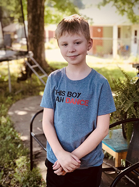 Austin Hasenohr is standing outside, grinning and wearing a grey shirt that reads, "this boy can dance."