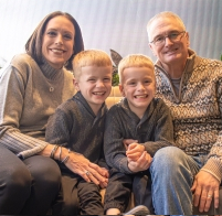 Family portrait of two adults and young twin boys seated together on a couch indoors.