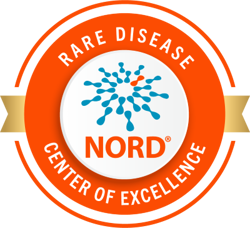 Circular badge with an orange border and gold ribbon. Inside, blue molecular-style graphic with one orange dot and the word NORD® in bold orange letters. Surrounding text reads Rare Disease Center of Excellence.