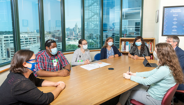 Several masked medical professionals sit at a conference table.