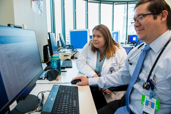 One male and one female physician look at a computer monitor together in an office setting.