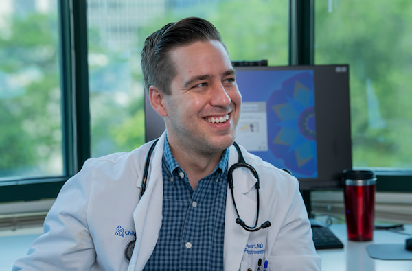 A photo of a smiling male physician in a white coat with a stethoscope around his neck.