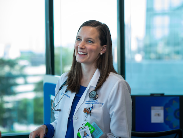 A photo of a smiling female physician with a lab coat and a stethoscope around her neck.