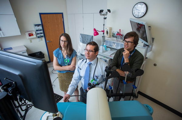 Three clinicians, two male and one female, look together at a computer monitor in a hospital room.