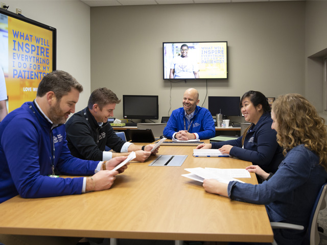 Five Sports Medicine fellows sitting around a table looking at papers and smiling