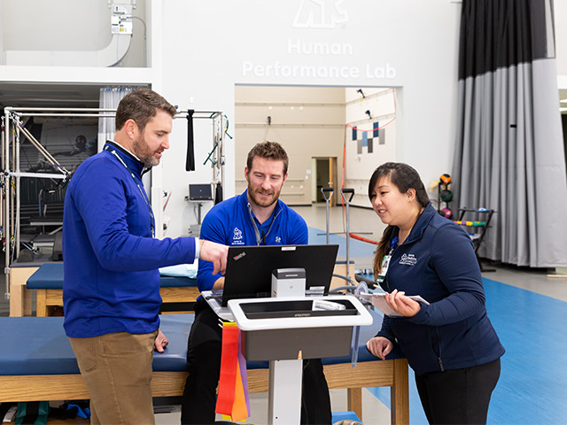 Three Sports Medicine fellows looking at laptop with PT equipment in background