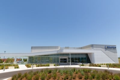 Exterior view of the Children’s Mercy Wichita facility with a white façade, large glass windows, landscaped greenery, and a clear blue sky.