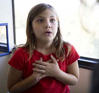 A young girl holds her hands to her chest and breathes in during an asthma doctor's appointment.