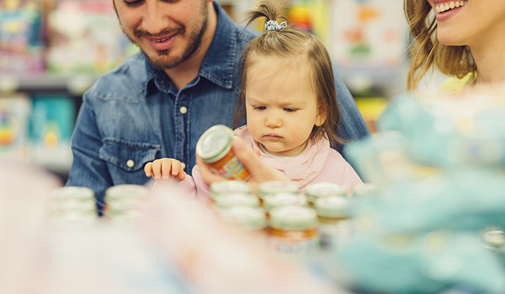 Family with young baby holding baby food jar in a grocery store.