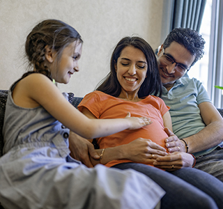 Young child touches mom's pregnant belly while sitting next to her and dad on the couch.