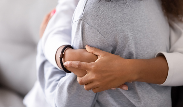 Close up of two torsos with arms hugging around a person.