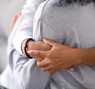 Close up of two torsos with arms hugging around a person.